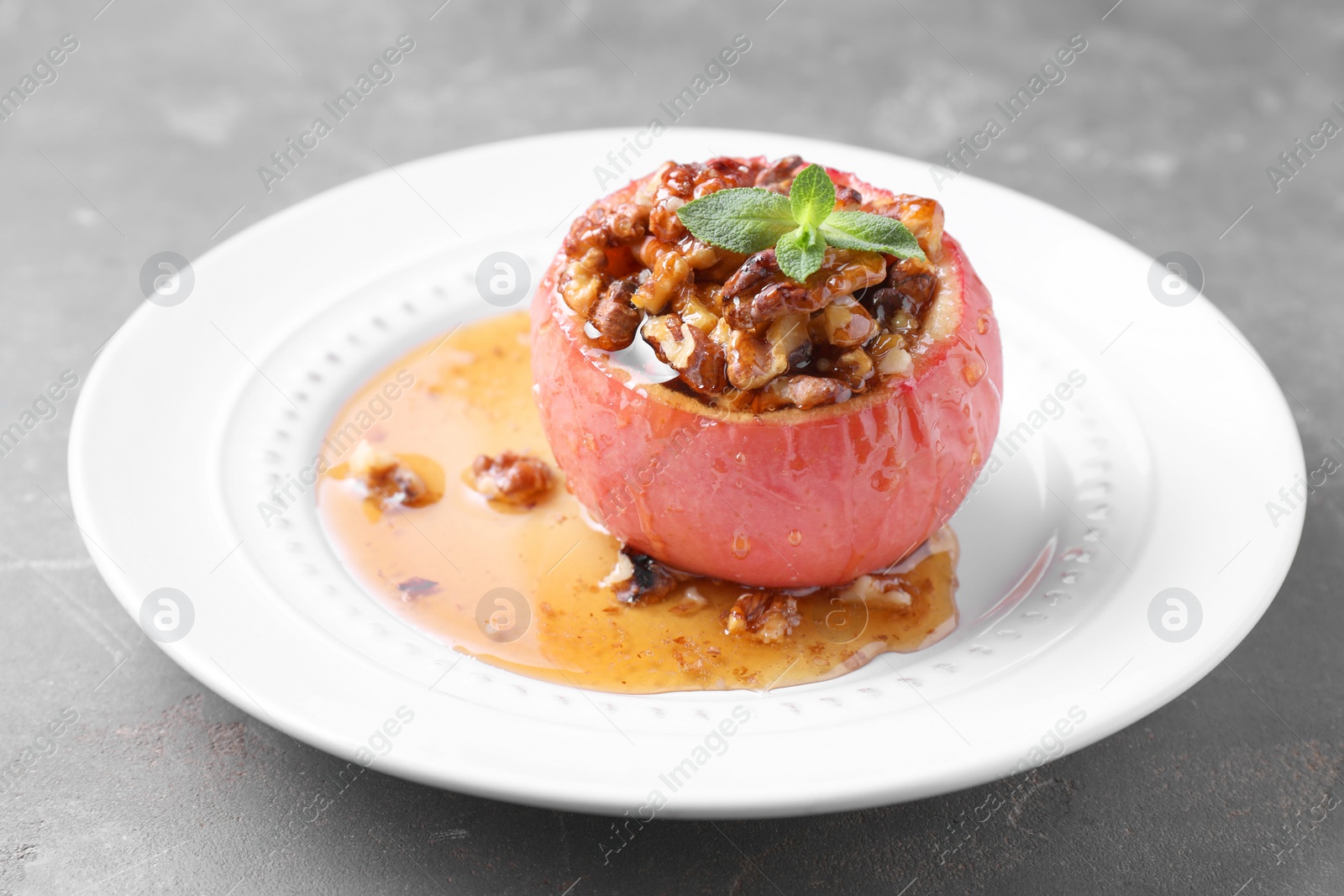 Photo of Tasty baked apple with nuts, honey and mint on gray table, closeup