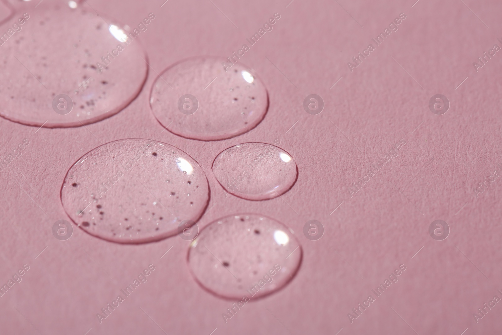 Photo of Drops of cosmetic serum on pink background, closeup. Space for text