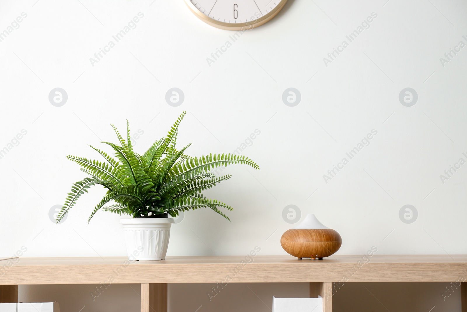 Photo of Modern aroma lamp and houseplant on wooden shelf near light wall