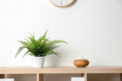 Photo of Modern aroma lamp and houseplant on wooden shelf near light wall