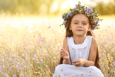 Photo of Cute little girl wearing flower wreath outdoors, space for text. Child spending time in nature
