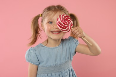 Happy girl covering eye with lollipop on pink background