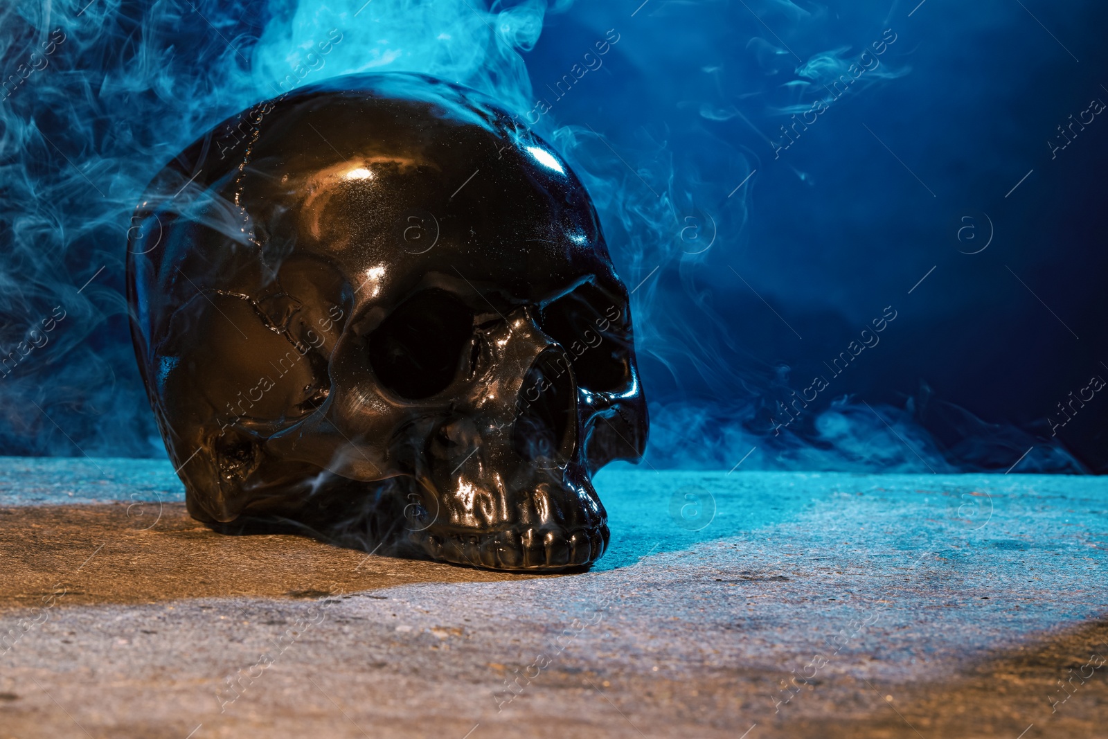 Photo of Black human skull and smoke on stone surface against color background. Space for text