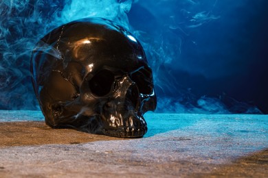 Photo of Black human skull and smoke on stone surface against color background. Space for text