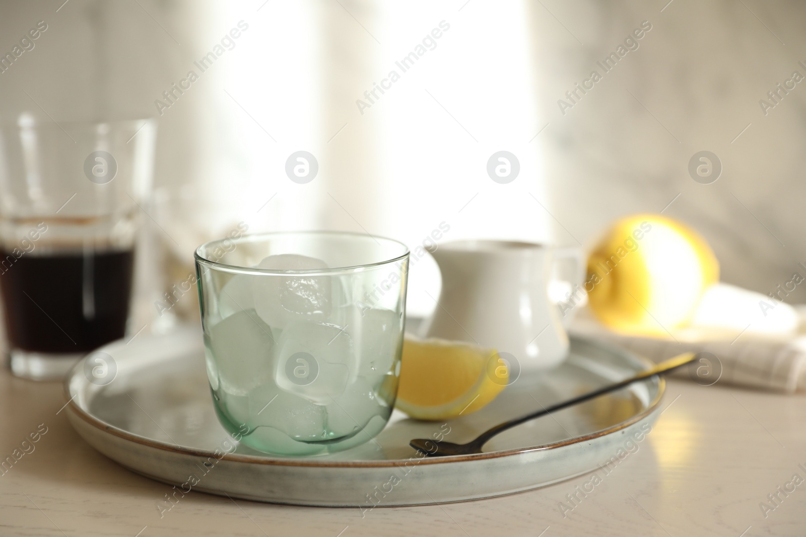 Photo of Making iced coffee. Ice cubes in glass and spoon on white wooden table, closeup