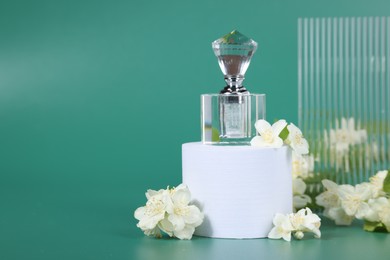 Presentation of aromatic perfume in bottle and beautiful jasmine flowers on green background, space for text