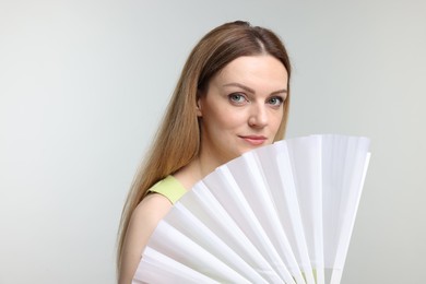 Beautiful woman with white hand fan on light grey background