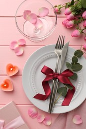 Photo of Place setting with heart shaped candles, bouquet of roses and gift on pink wooden table, flat lay. Romantic dinner