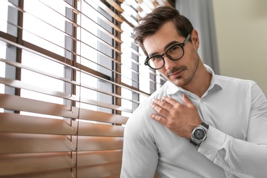 Photo of Handsome young man in white shirt with glasses standing near window indoors