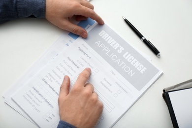 Man with driver's license application form at white table, above view