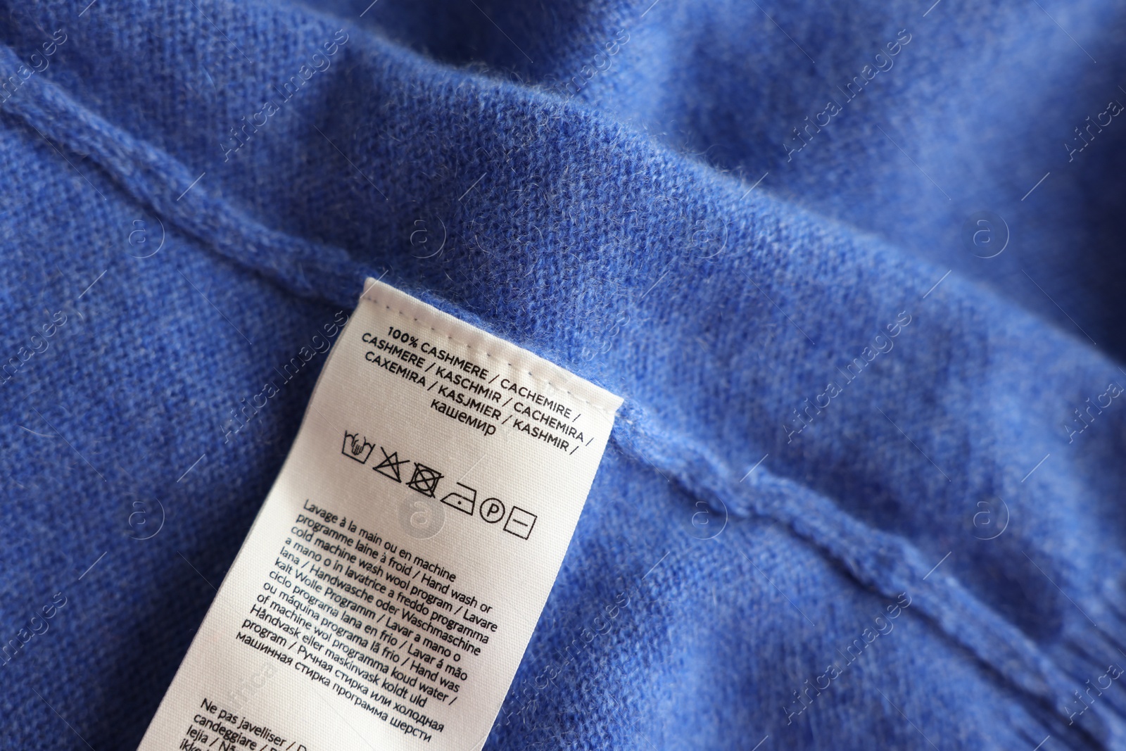 Photo of Clothing label in different languages on blue garment, top view