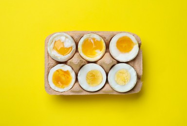 Photo of Boiled chicken eggs of different readiness stages in carton on yellow background, top view