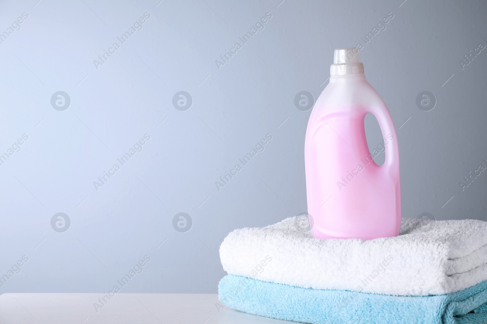 Photo of Bottle of laundry detergent and towels on table, space for text