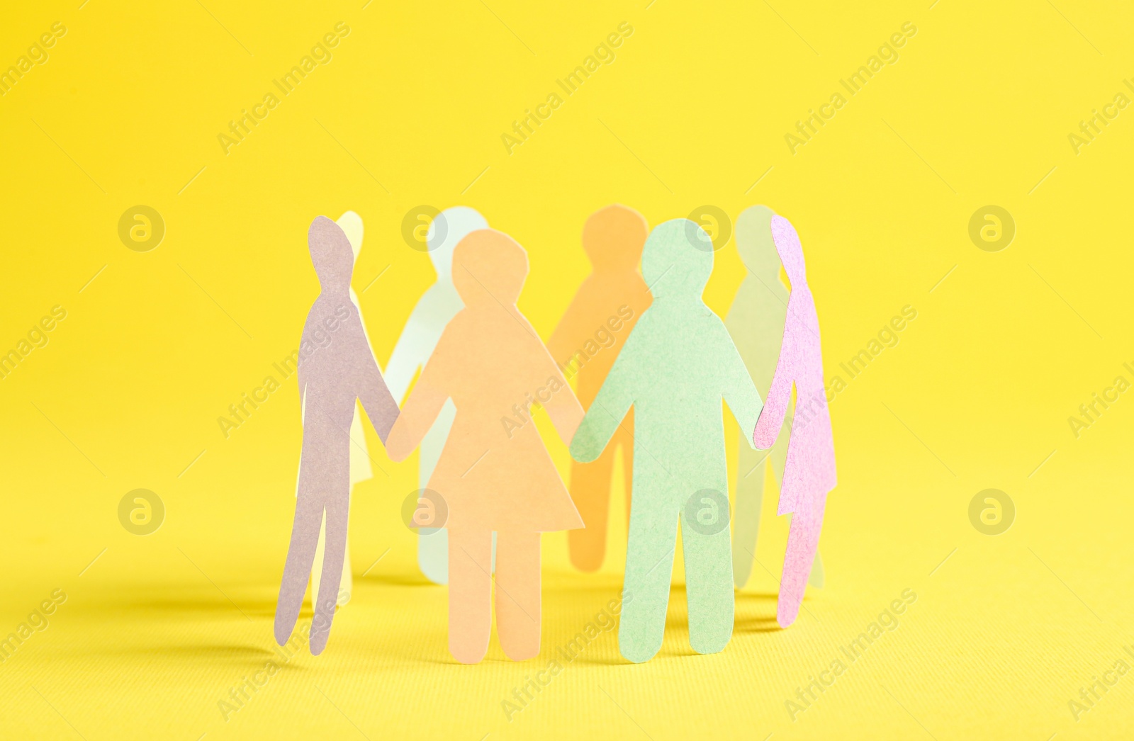 Photo of Many different paper human figures standing in circle on yellow background. Diversity and inclusion concept