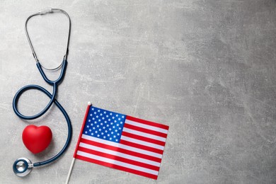 Photo of American flag, heart and stethoscope on light grey table, flat lay. Space for text
