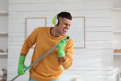 Photo of Man in headphones with mop singing while cleaning at home