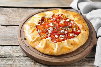 Photo of Tasty galette with tomato, thyme and cheese (Caprese galette) on wooden table, closeup. Space for text