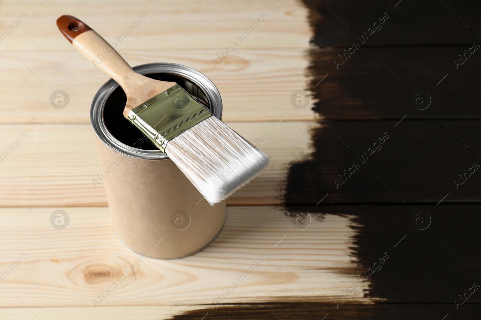 Photo of Can and brush with wood stain on wooden surface. Space for text