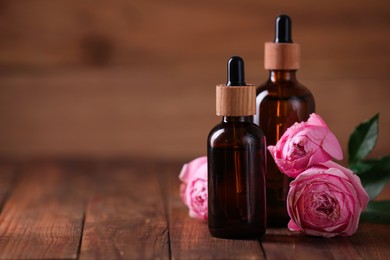 Photo of Bottles of essential rose oil and flowers on wooden table, space for text
