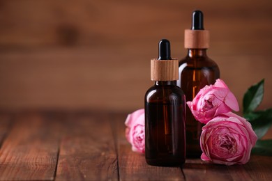 Bottles of essential rose oil and flowers on wooden table, space for text