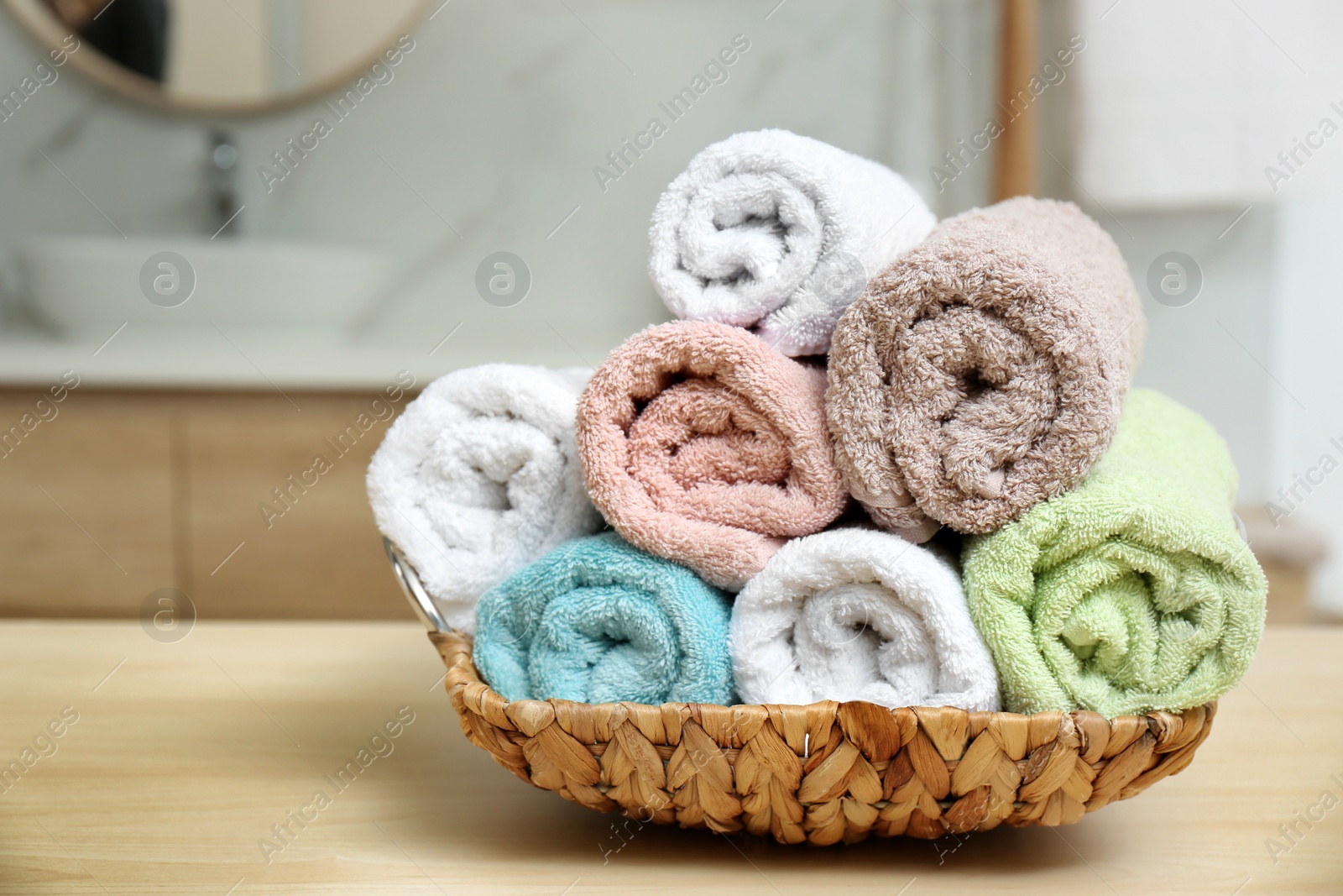 Photo of Rolled color towels on wooden table in bathroom, closeup