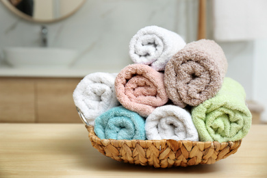 Photo of Rolled color towels on wooden table in bathroom, closeup