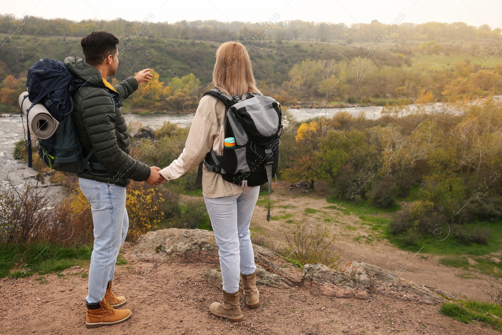 Photo of Couple of travelers with backpacks enjoying beautiful view near mountain river. Autumn vacation