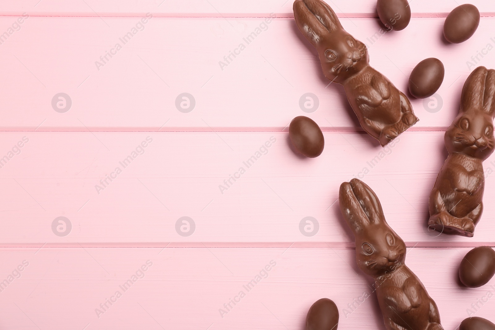 Photo of Chocolate Easter bunny and eggs on pink wooden table, flat lay. Space for text