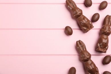 Chocolate Easter bunny and eggs on pink wooden table, flat lay. Space for text