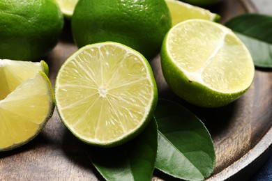 Photo of Fresh ripe limes and leaves on table, closeup