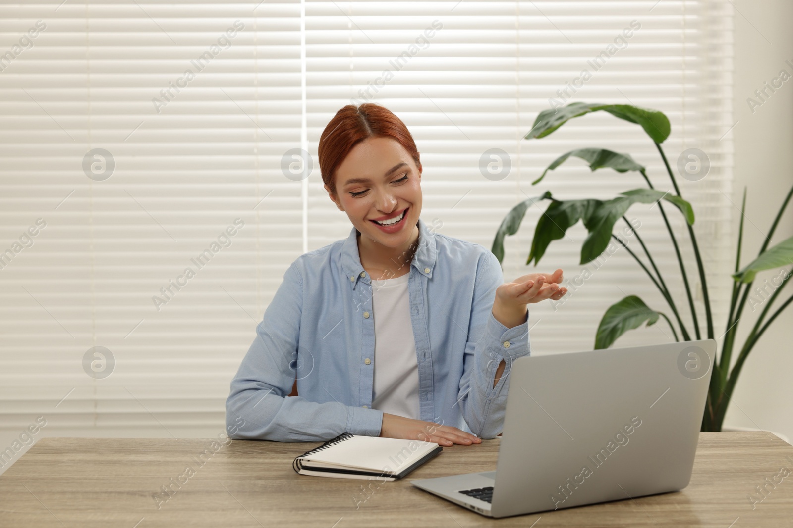 Photo of Young woman having video chat via laptop at wooden table indoors