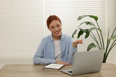 Photo of Young woman having video chat via laptop at wooden table indoors