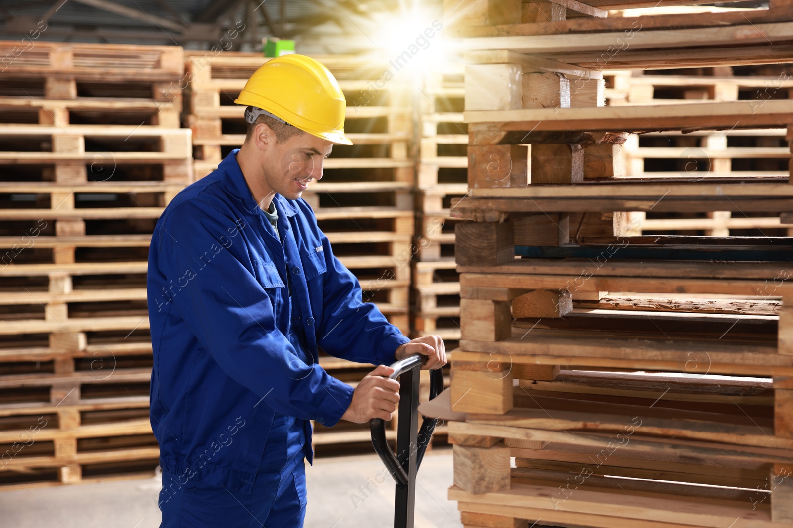 Image of Worker moving wooden pallets with manual forklift in warehouse