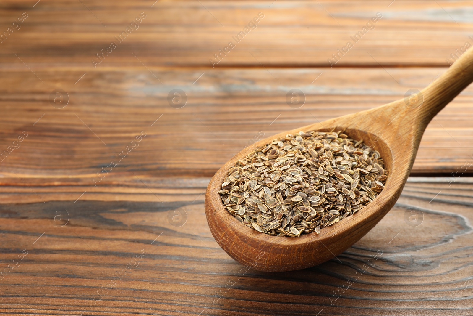 Photo of Spoon of dry dill seeds on wooden table, closeup. Space for text