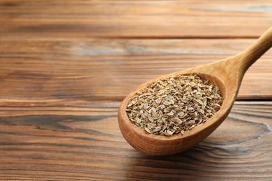 Spoon of dry dill seeds on wooden table, closeup. Space for text