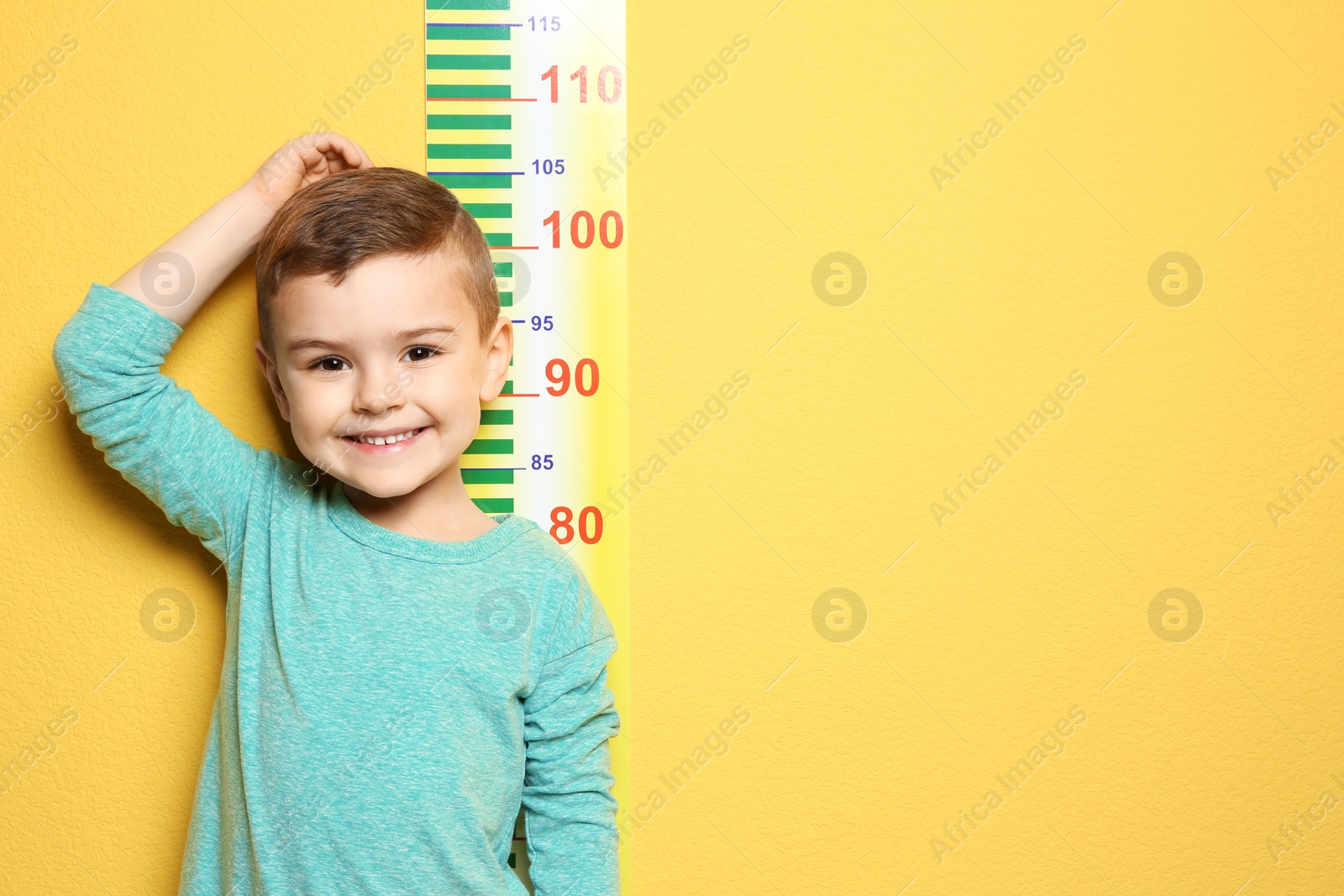 Photo of Little boy measuring his height on color background
