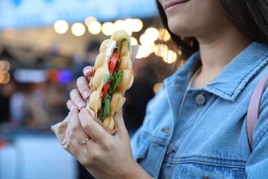Photo of Young woman holding delicious bubble waffle with tomato and arugula outdoors, closeup