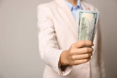 Young woman holding dollar bills on light grey background, closeup