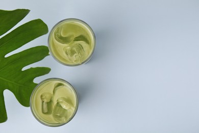 Photo of Glasses of tasty iced matcha latte and leaf on light grey background, flat lay. Space for text
