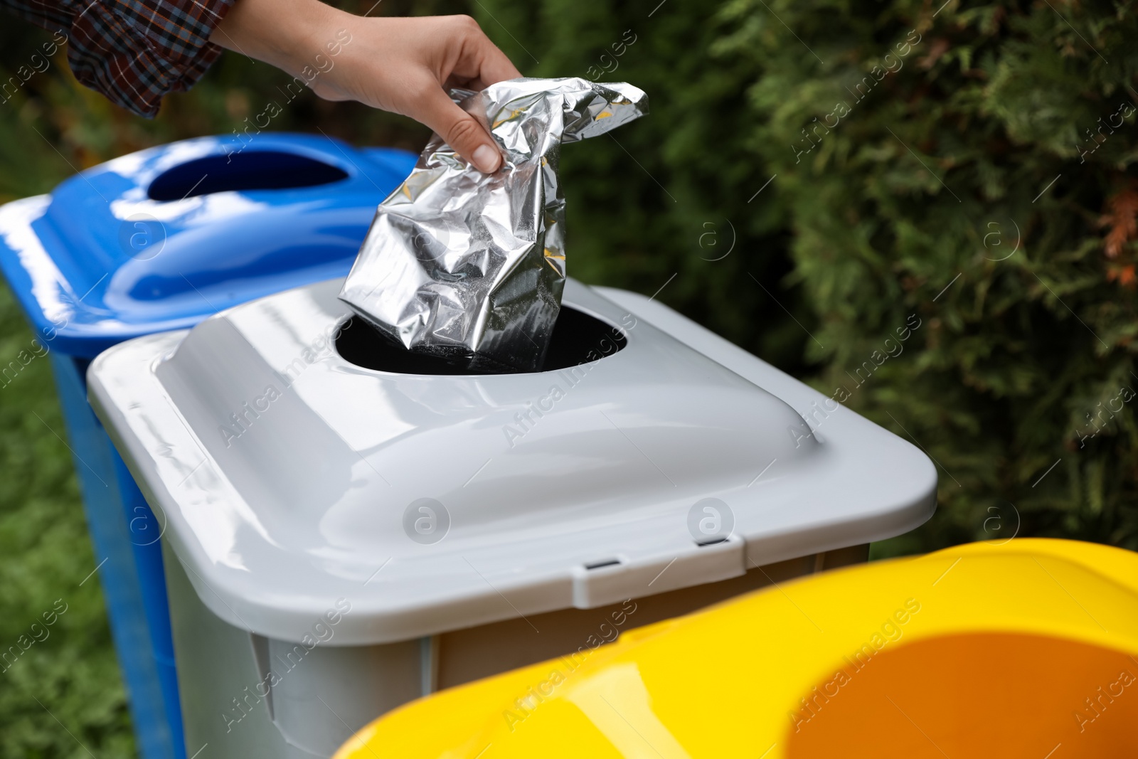 Photo of Woman throwing foil package into recycling bin outdoors, closeup