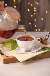 Photo of Woman pouring aromatic tea into cup at light wooden table, closeup