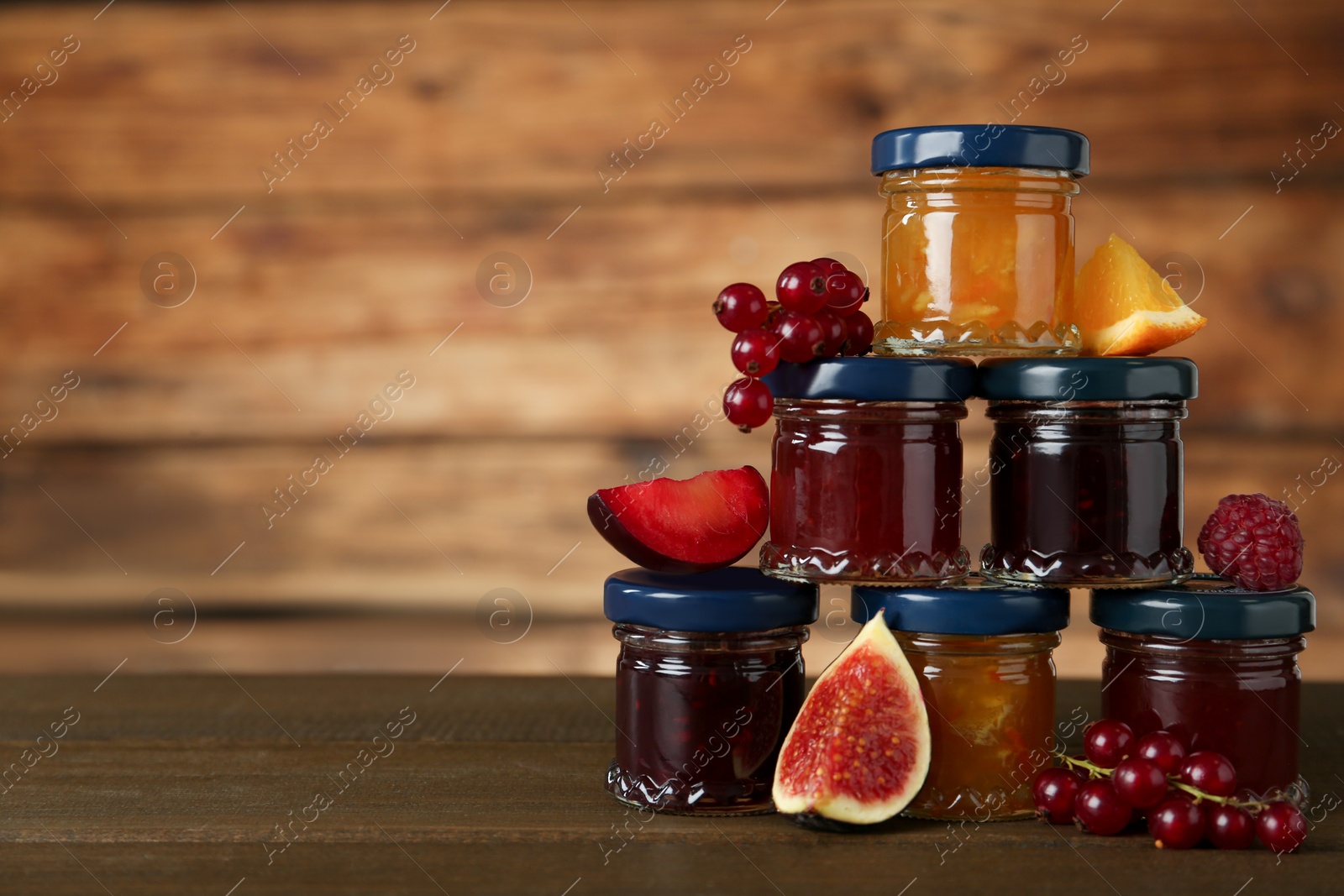 Photo of Jars of different jams and fresh ingredients on wooden table, space for text