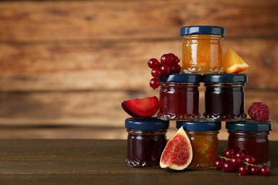Photo of Jars of different jams and fresh ingredients on wooden table, space for text