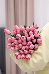 Photo of Woman holding bouquet of pink tulips indoors, closeup