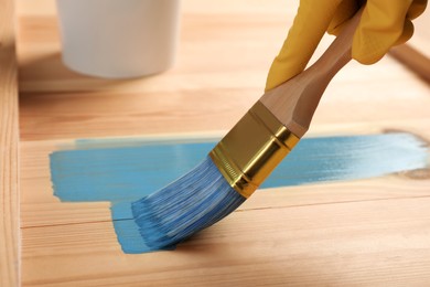 Photo of Worker applying blue paint onto wooden surface, closeup