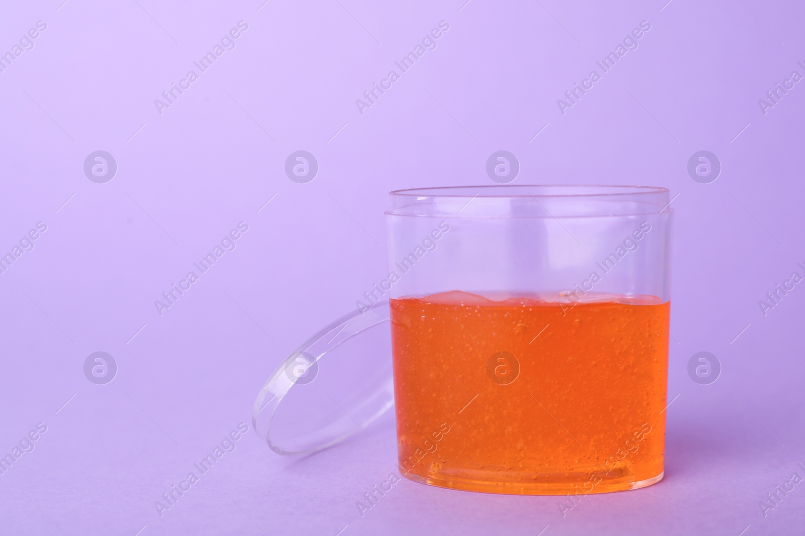 Photo of Orange slime in plastic container on violet background. Space for text