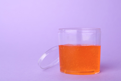 Orange slime in plastic container on violet background. Space for text