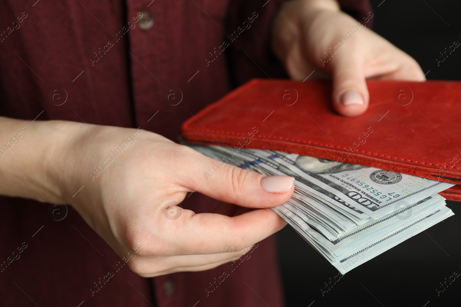 Photo of Money exchange. Woman putting dollar banknotes into wallet on dark background, closeup