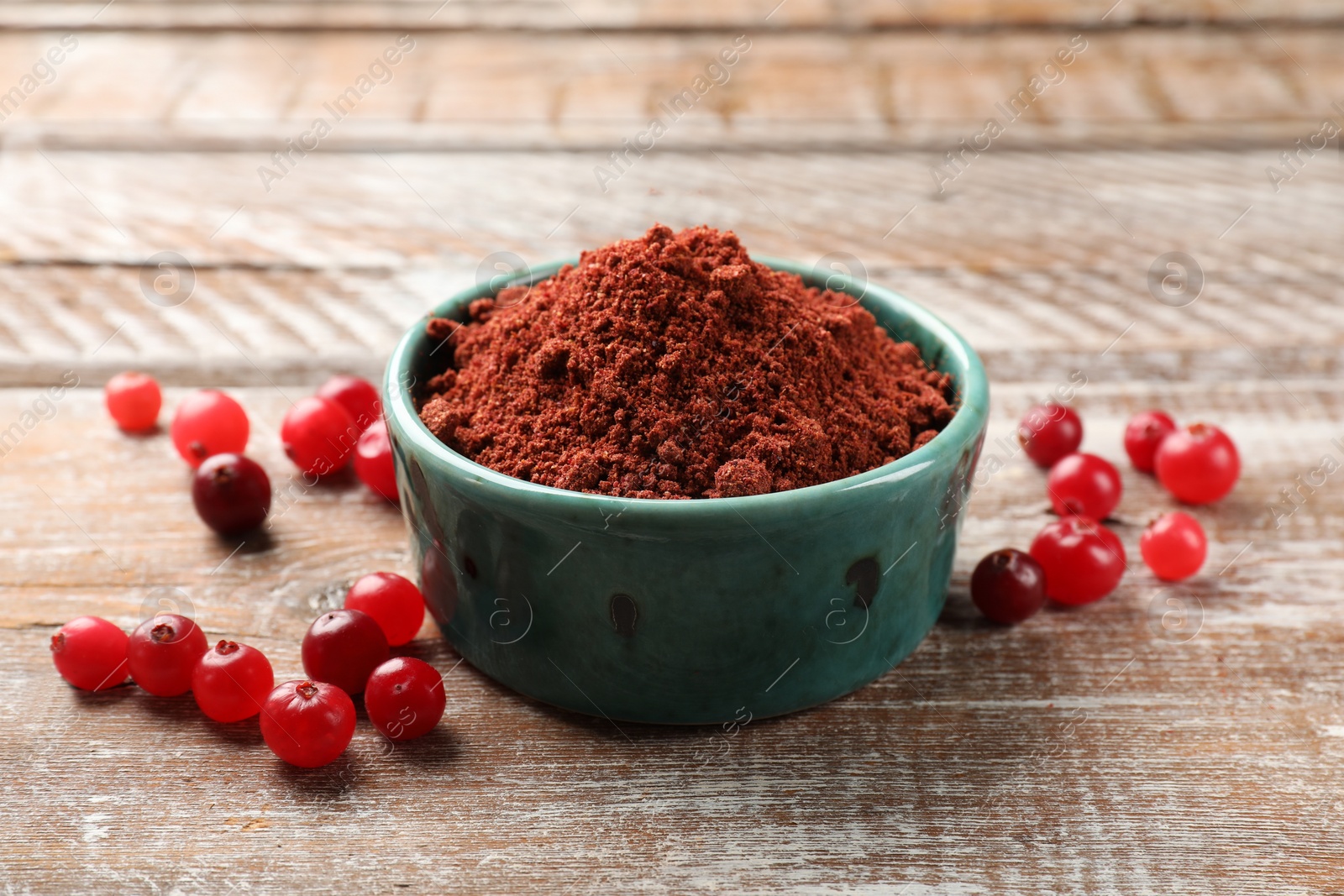 Photo of Cranberry powder in bowl and fresh berries on wooden rustic table, closeup