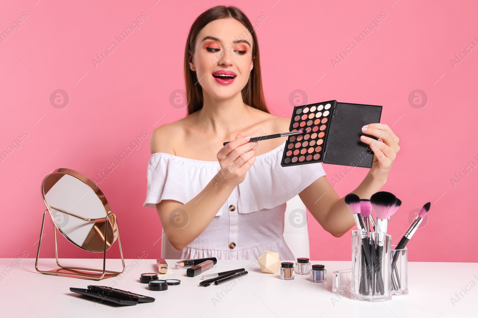 Photo of Beauty blogger with brush and eyeshadow palette on pink background